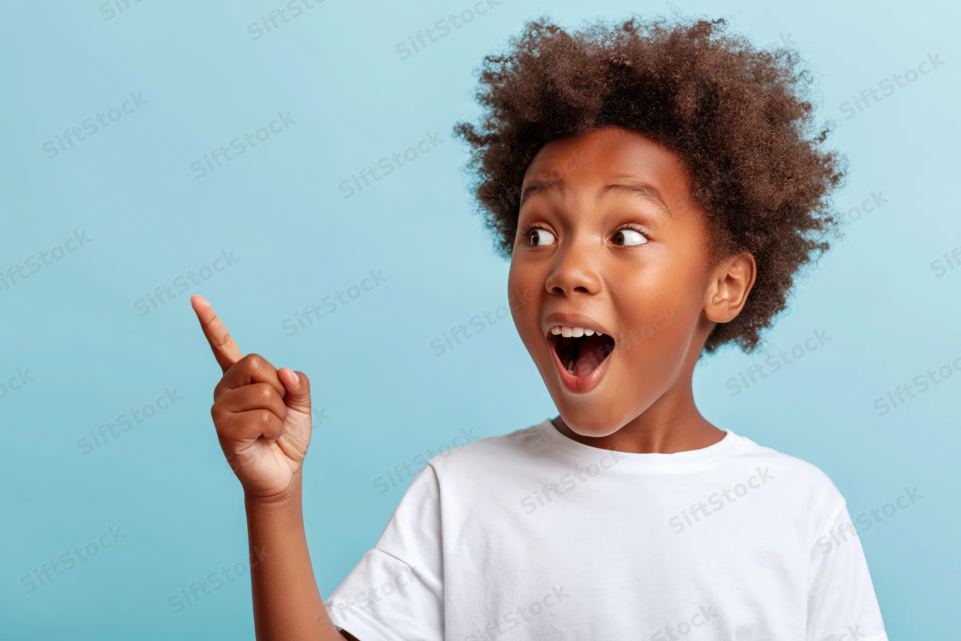Excited young black boy pointing upward with open mouth against blue background
