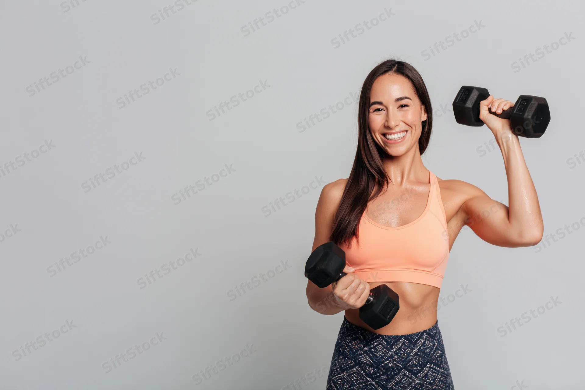 Woman lifting dumbbells smiling at camera in sportswear against gray background