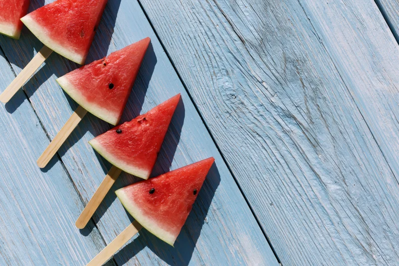 Triangular watermelon slices on wooden sticks arranged on a blue weathered wooden surface
