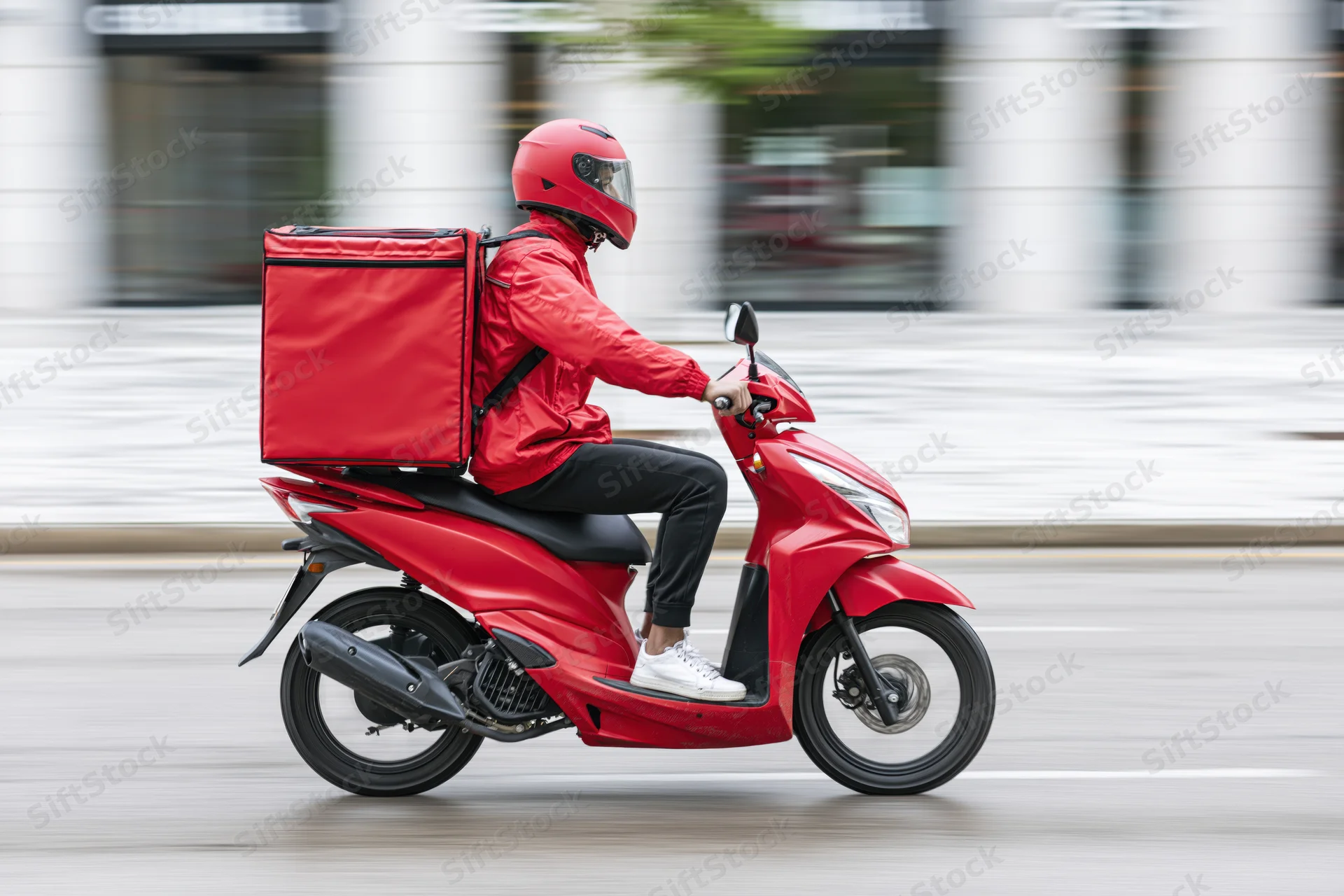 Delivery rider on red scooter moving through urban street