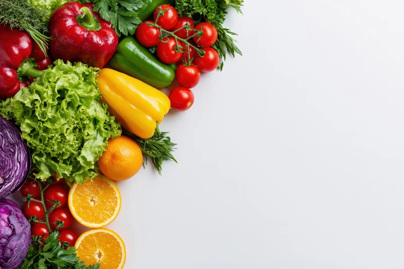 Fresh vegetables and fruits arranged along the left side on a white surface
