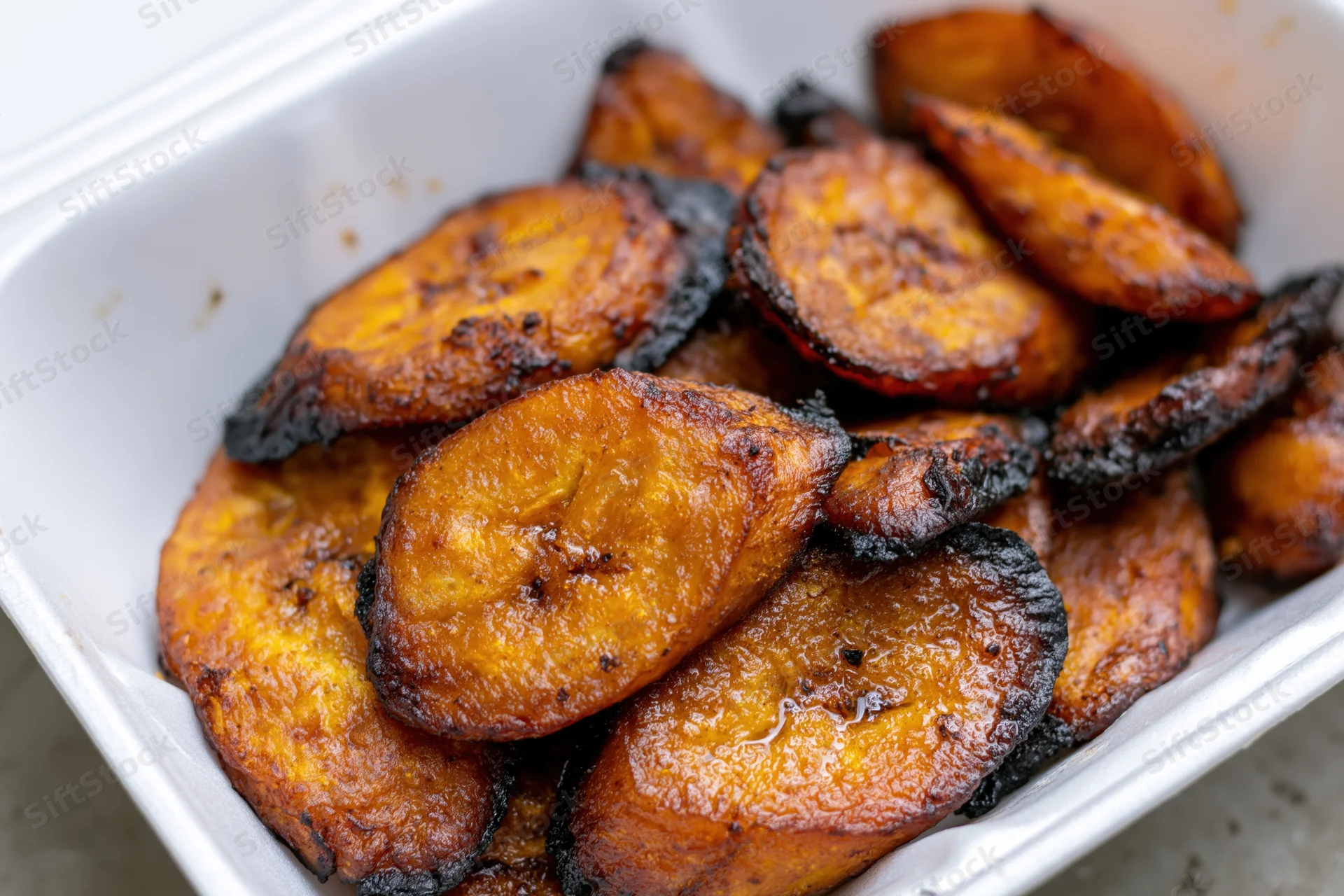Fried sweet plantain slices piled in a white styrofoam container
