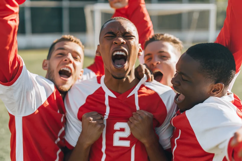 Four soccer players celebrating victory on the field in red and white jerseys