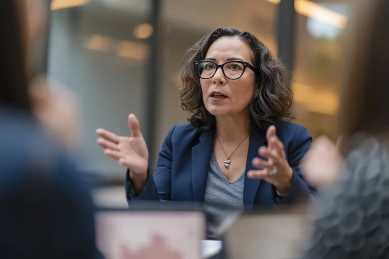 Woman in business attire gesturing while speaking during a meeting in an office setting