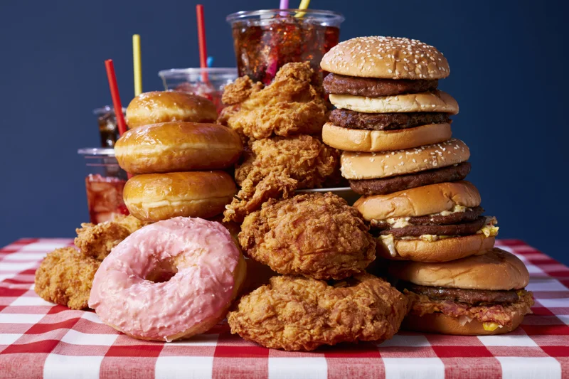 Pile of burgers, donuts, fried chicken and soda on a red and white checkered tablecloth