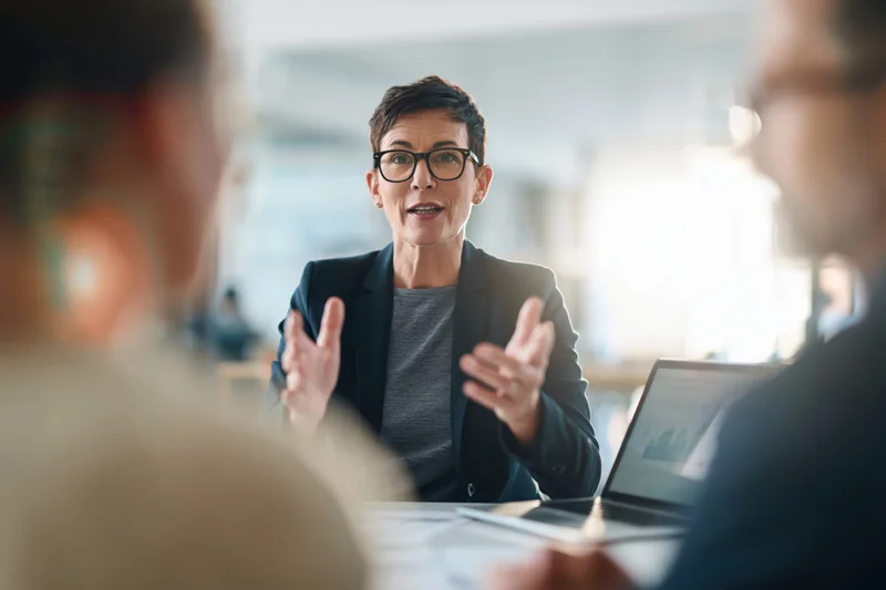 Businesswoman leading discussion at office meeting with colleagues around table