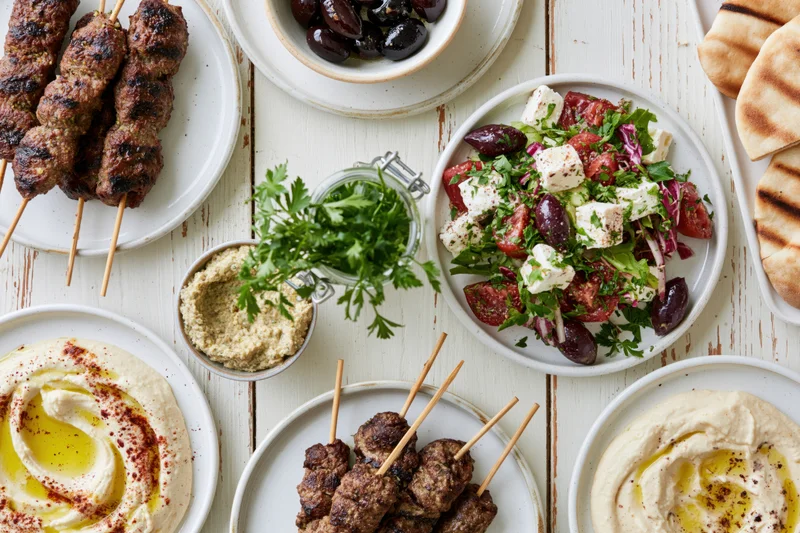 Mediterranean mezze spread with hummus, kebabs, salad and pita on a white wooden table