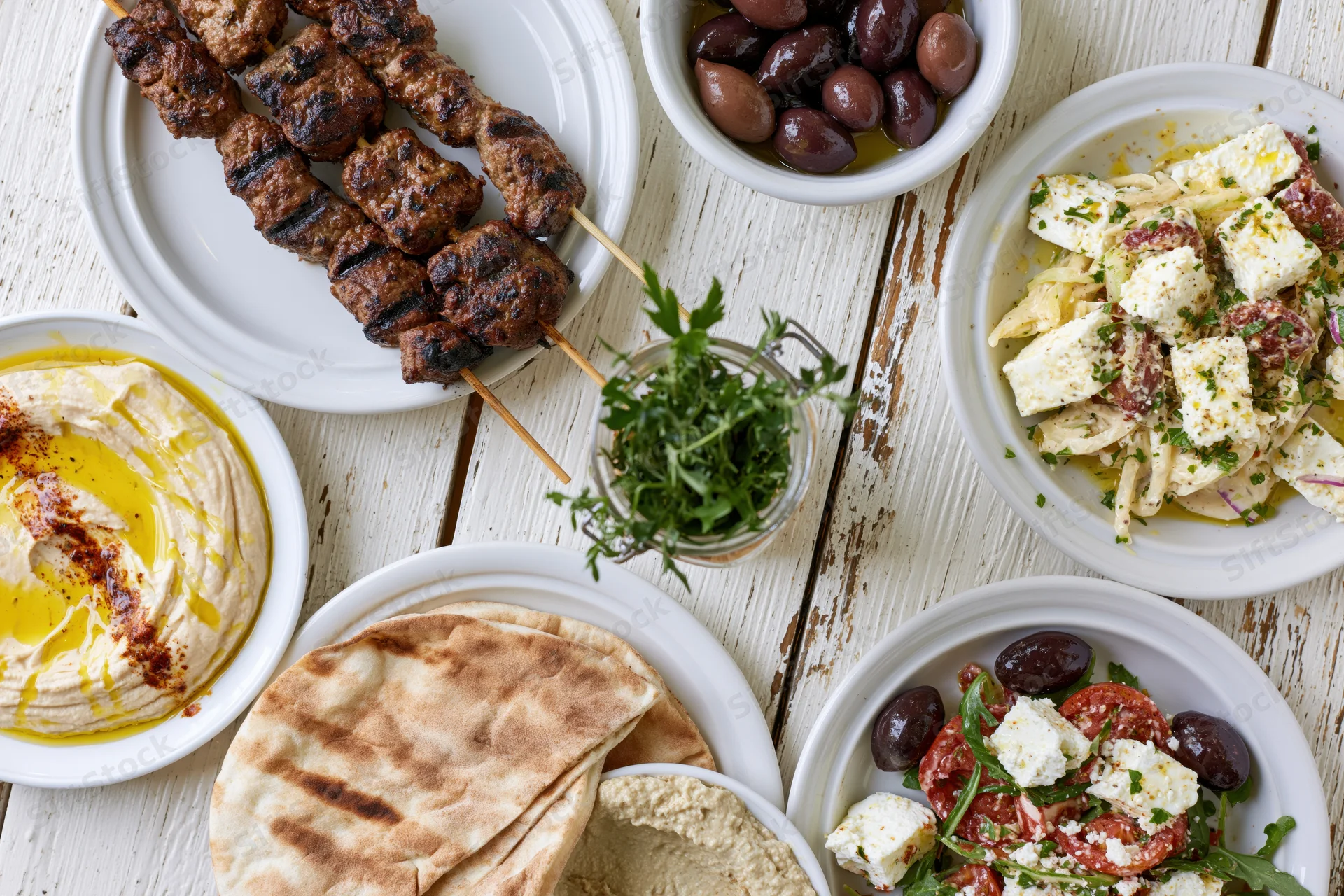 Mediterranean mezze spread with grilled kebabs, hummus, feta salads, and flatbread on a white wooden table