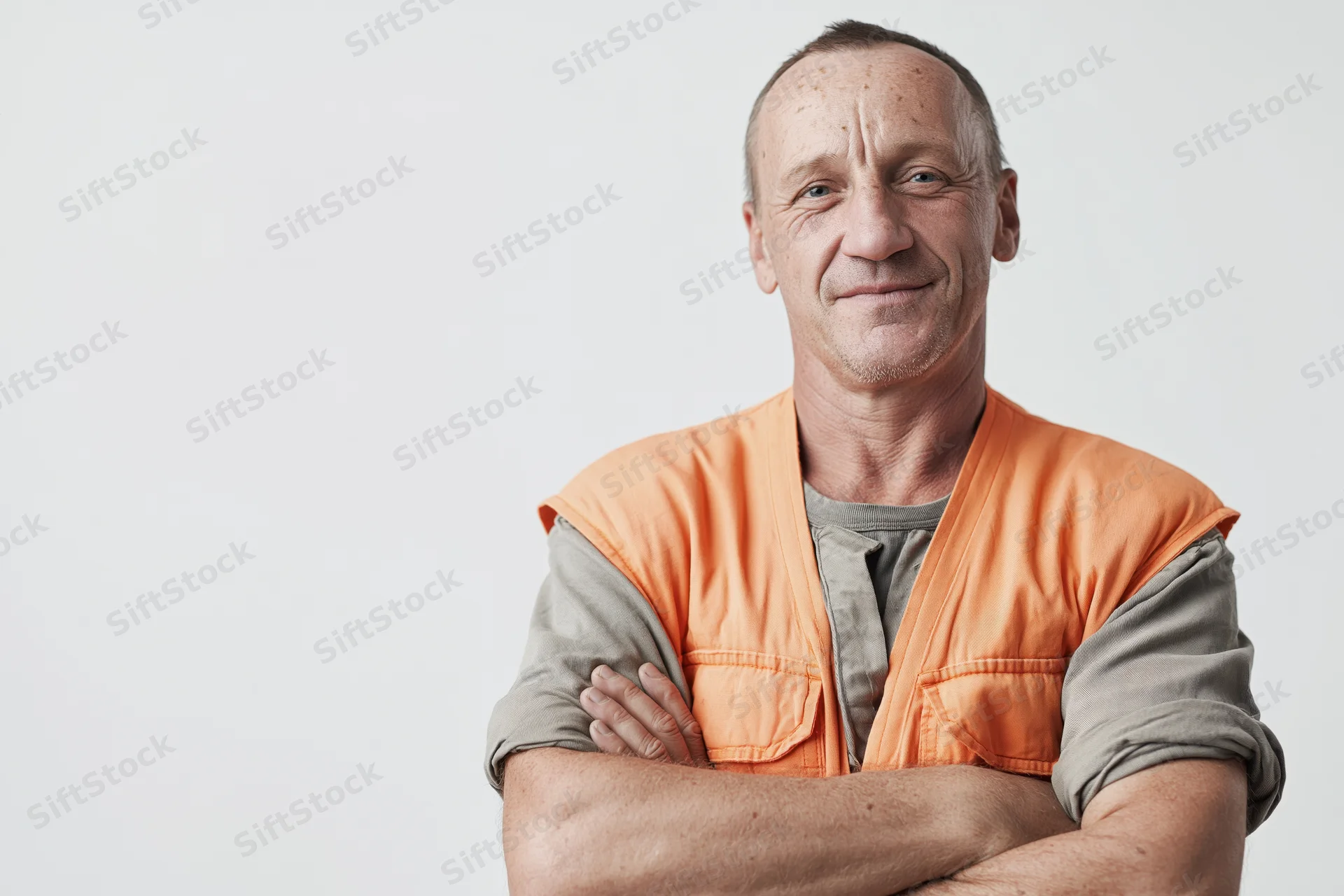 Middle-aged construction worker with arms crossed and gentle smile in studio portrait