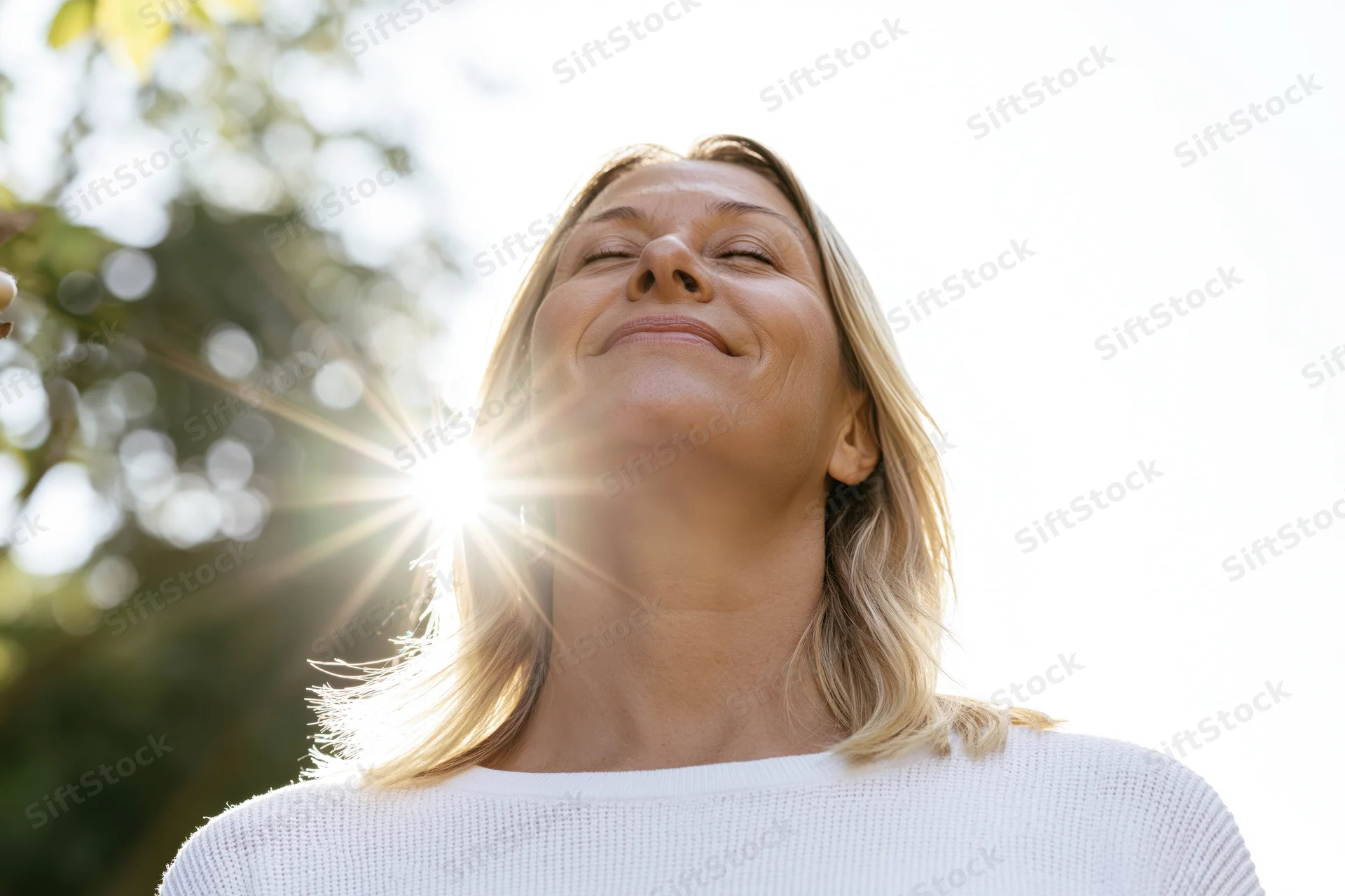 Middle-aged woman with blonde hair smiling with eyes closed in sunlight outdoors