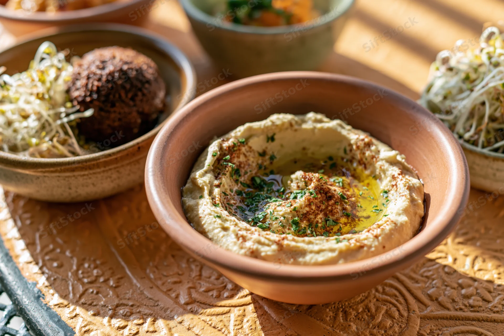 Hummus in a clay bowl with falafel and sprouts on a decorated metal tray