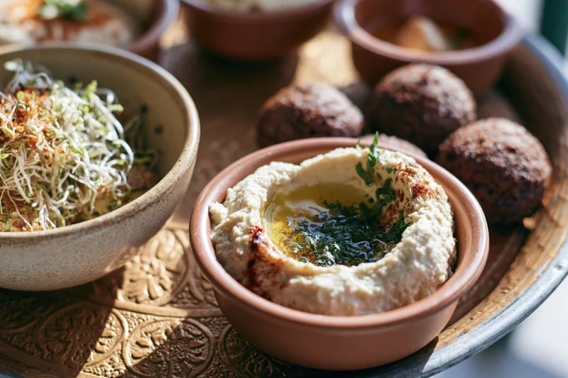 Hummus in a clay bowl with falafel and sprouts on a decorated metal tray