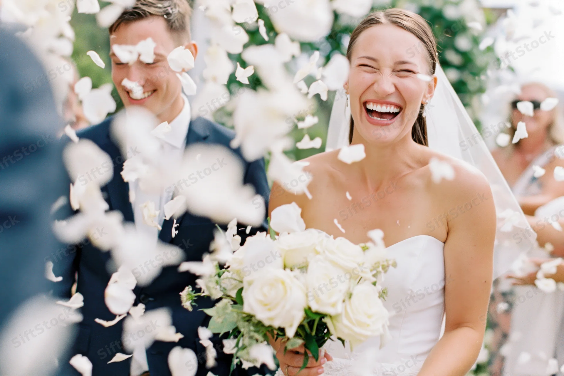Bride and groom laughing as flower petals fall around them outdoors