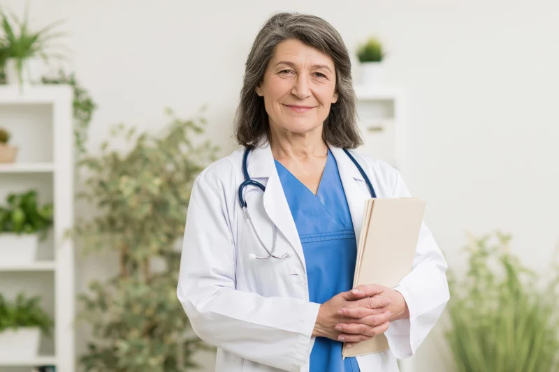Woman doctor in white coat holding folder in clinic office with plants in background