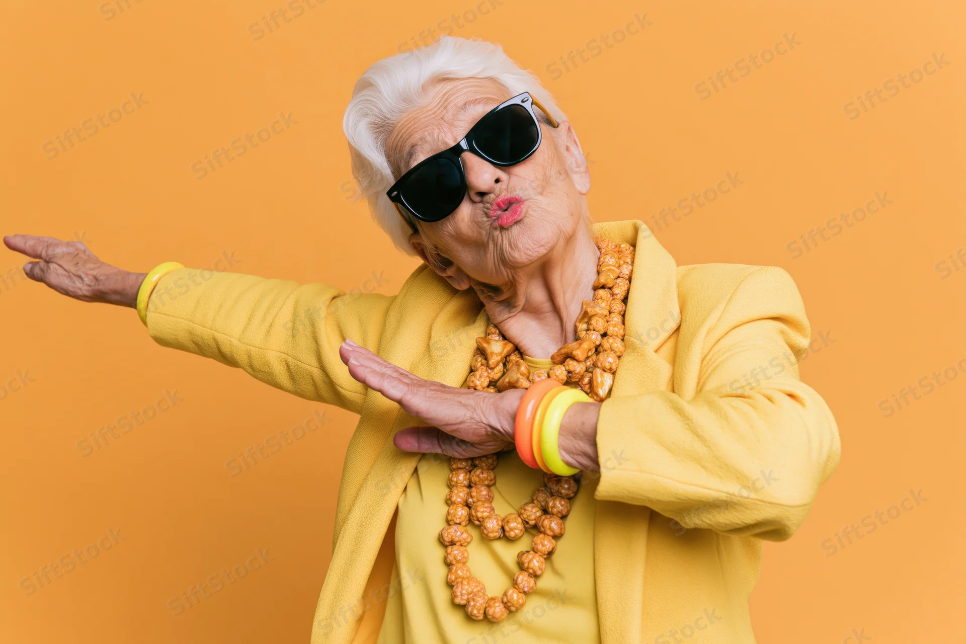 Senior woman dabbing in yellow jacket and sunglasses against orange background
