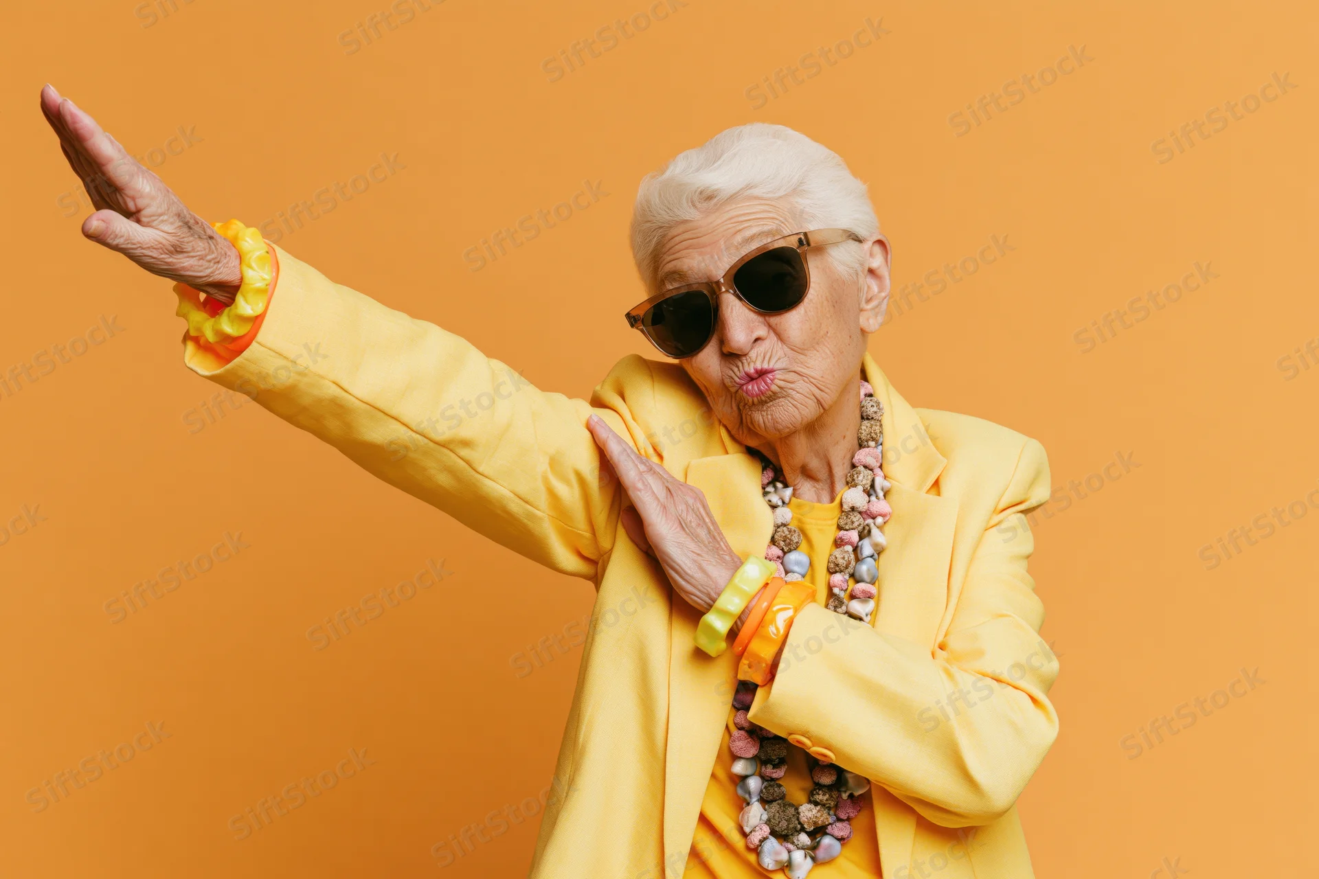 Senior woman dabbing in yellow jacket and sunglasses against orange background