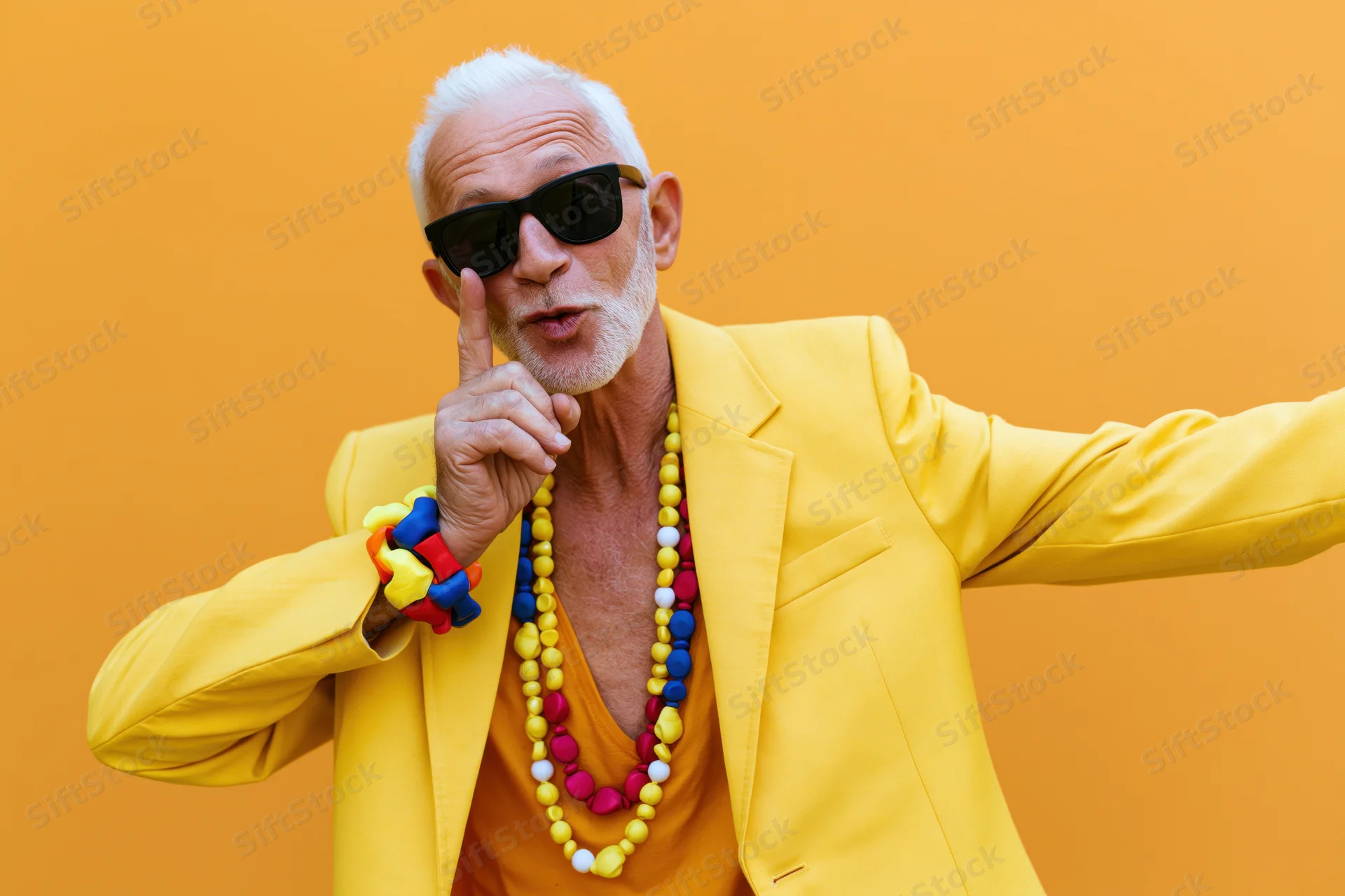 Senior man in yellow jacket and colorful beads dabbing against orange background