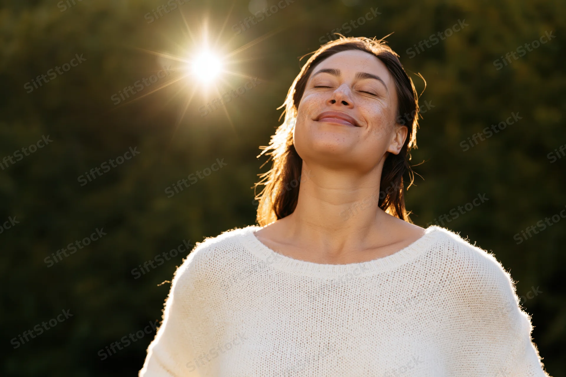 Woman smiling with eyes closed in sunlight outdoors