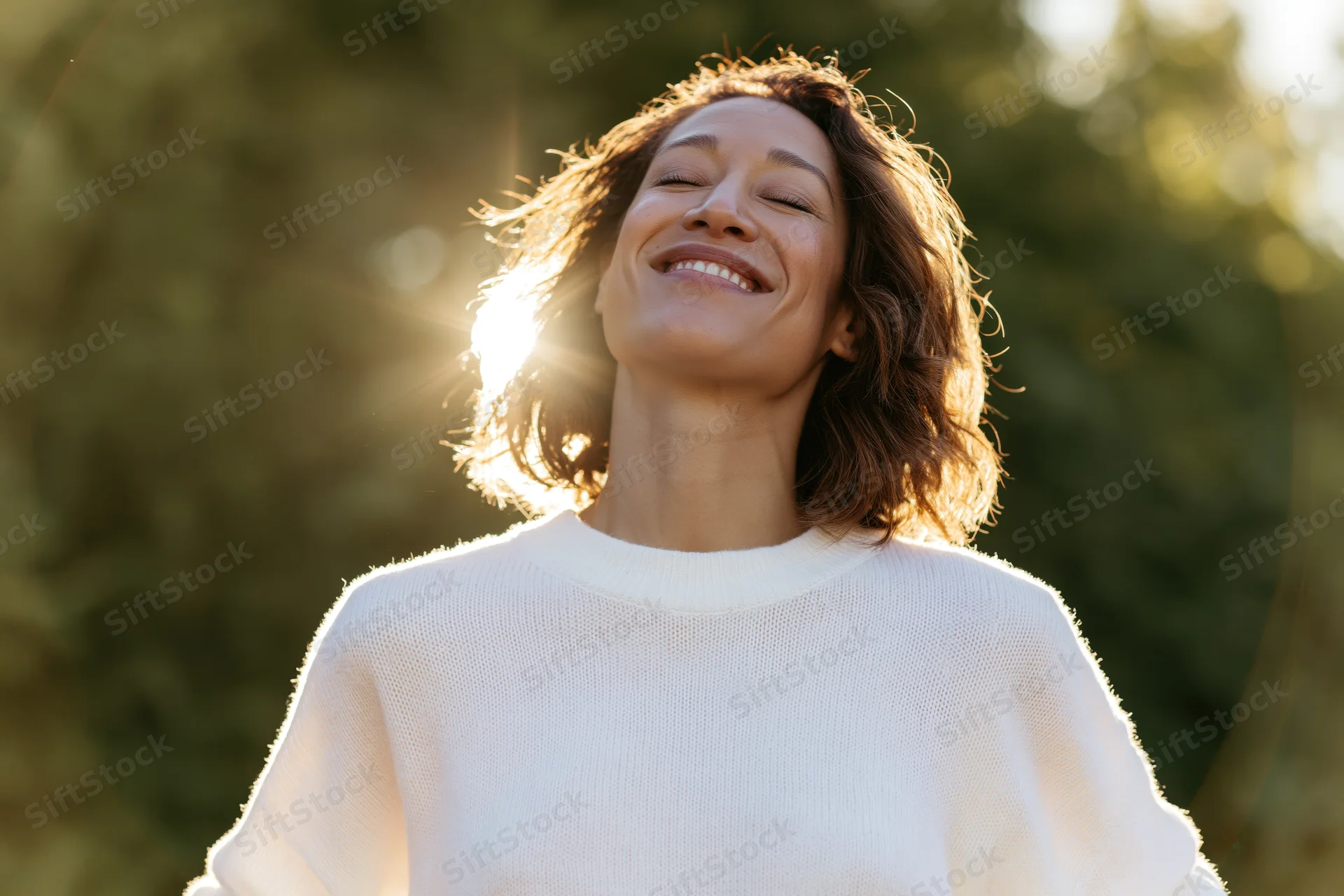 Woman smiling with eyes closed outdoors in sunlight