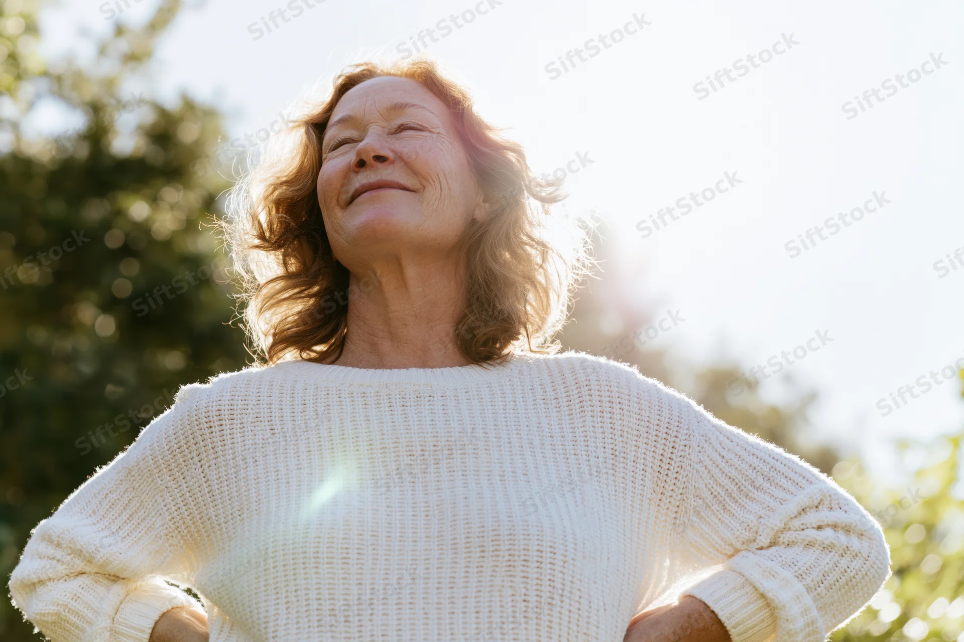 Senior woman smiling with eyes closed in sunlight outdoors