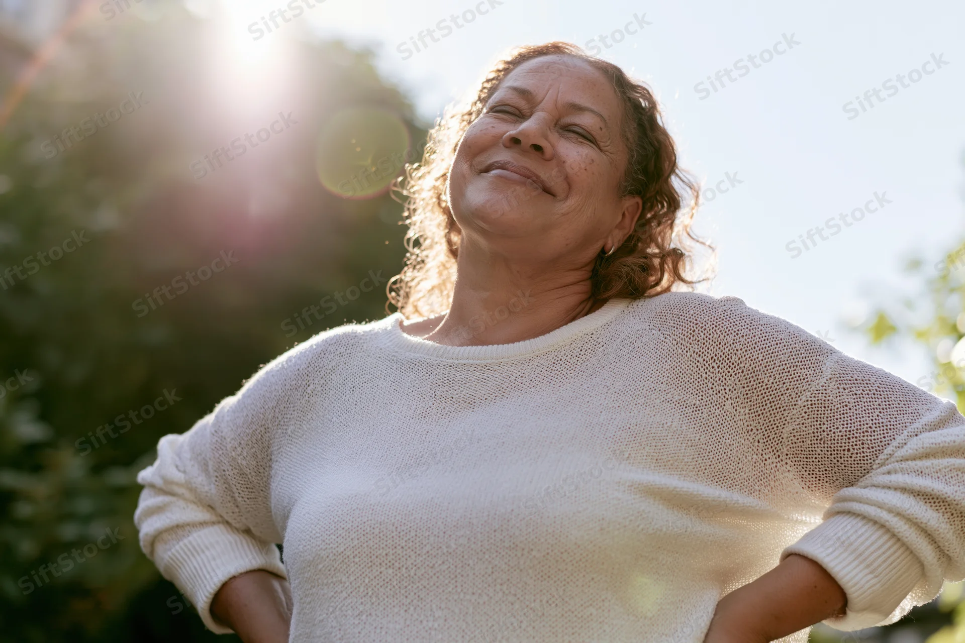 Senior woman smiling with hands on hips outdoors in sunlight