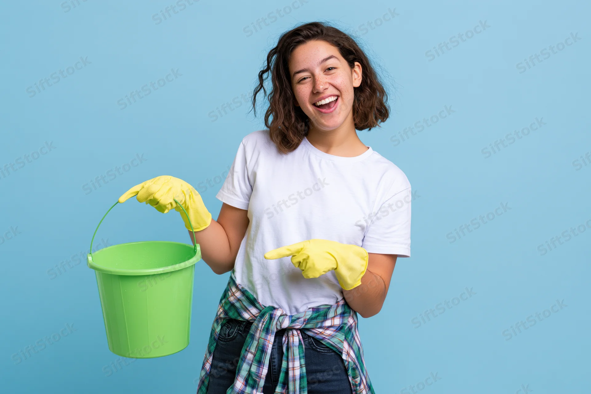 Woman holding green bucket and pointing with gloved hand against blue background