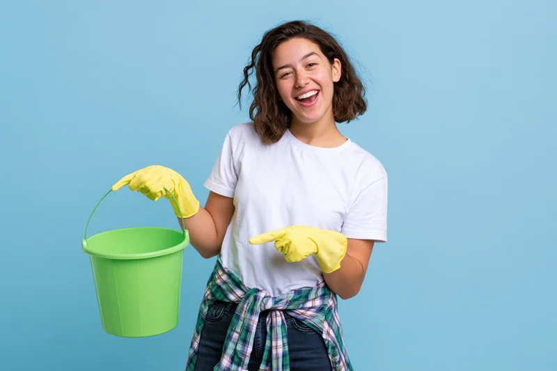 Woman holding green bucket and pointing with gloved hand against blue background