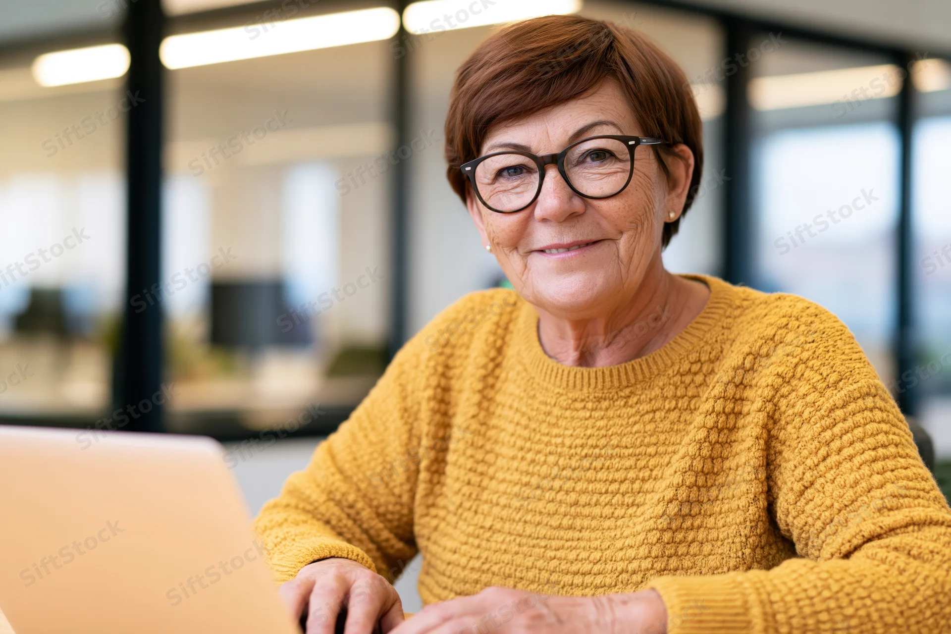 Senior woman smiling while working on laptop in modern office setting