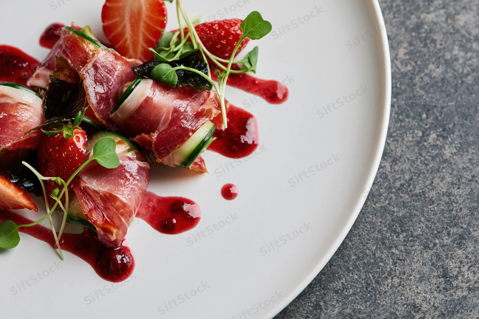 Prosciutto-wrapped appetizer with strawberries and microgreens on a white plate