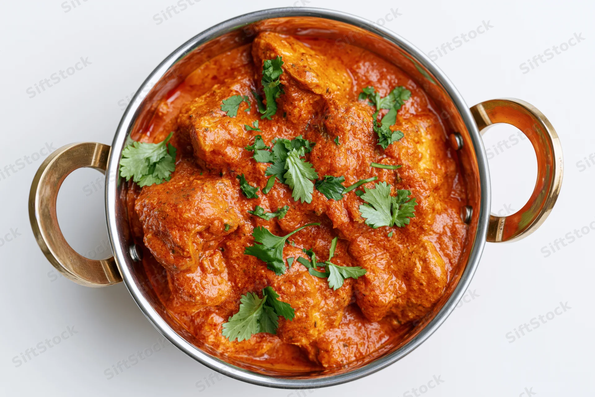 Butter chicken curry in a stainless steel balti bowl with cilantro garnish, overhead view on white background
