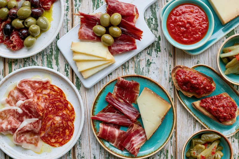 Spanish tapas spread with cured meats, cheese, olives and sauces arranged on a rustic wooden table