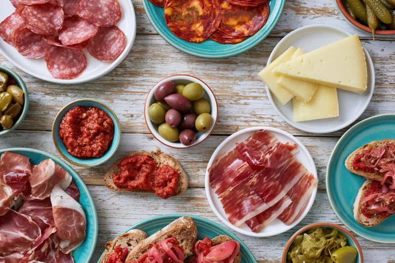 Spanish tapas spread with cured meats, cheese, olives and bread on a rustic wooden table