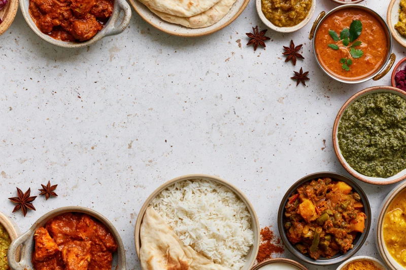 Assorted indian dishes arranged in a flat lay around a white surface with copyspace in center