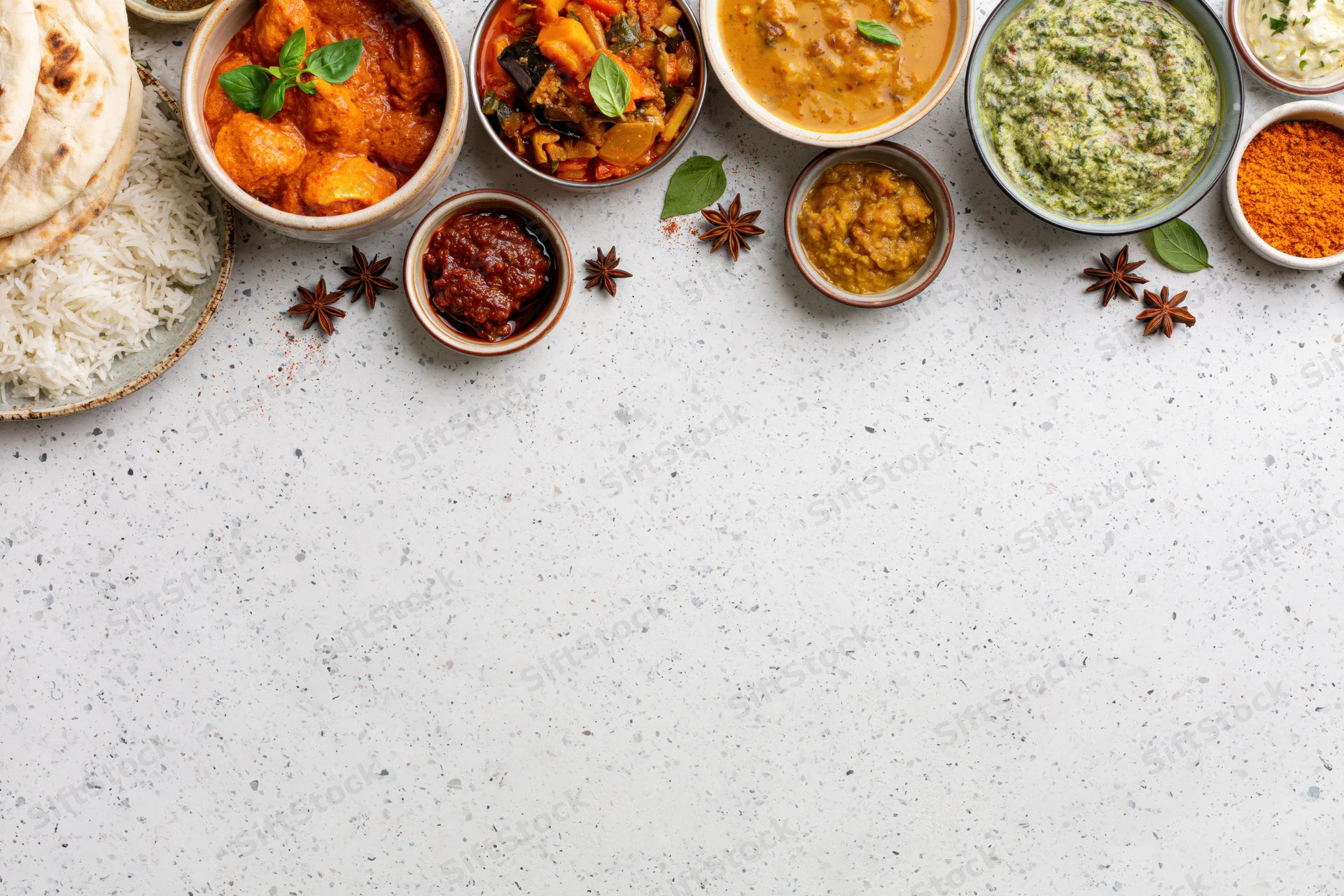 Assorted indian dishes arranged in bowls and plates along the top of a white speckled countertop with copyspace below