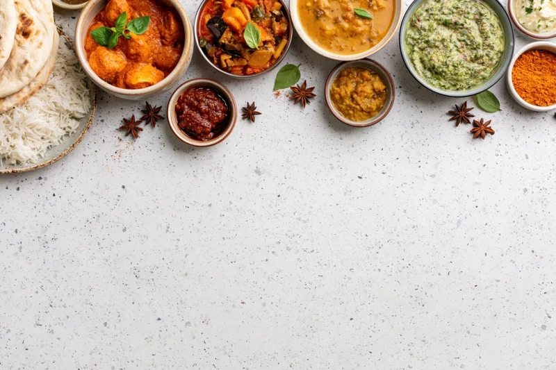 Assorted indian dishes arranged in bowls and plates along the top of a white speckled countertop with copyspace below