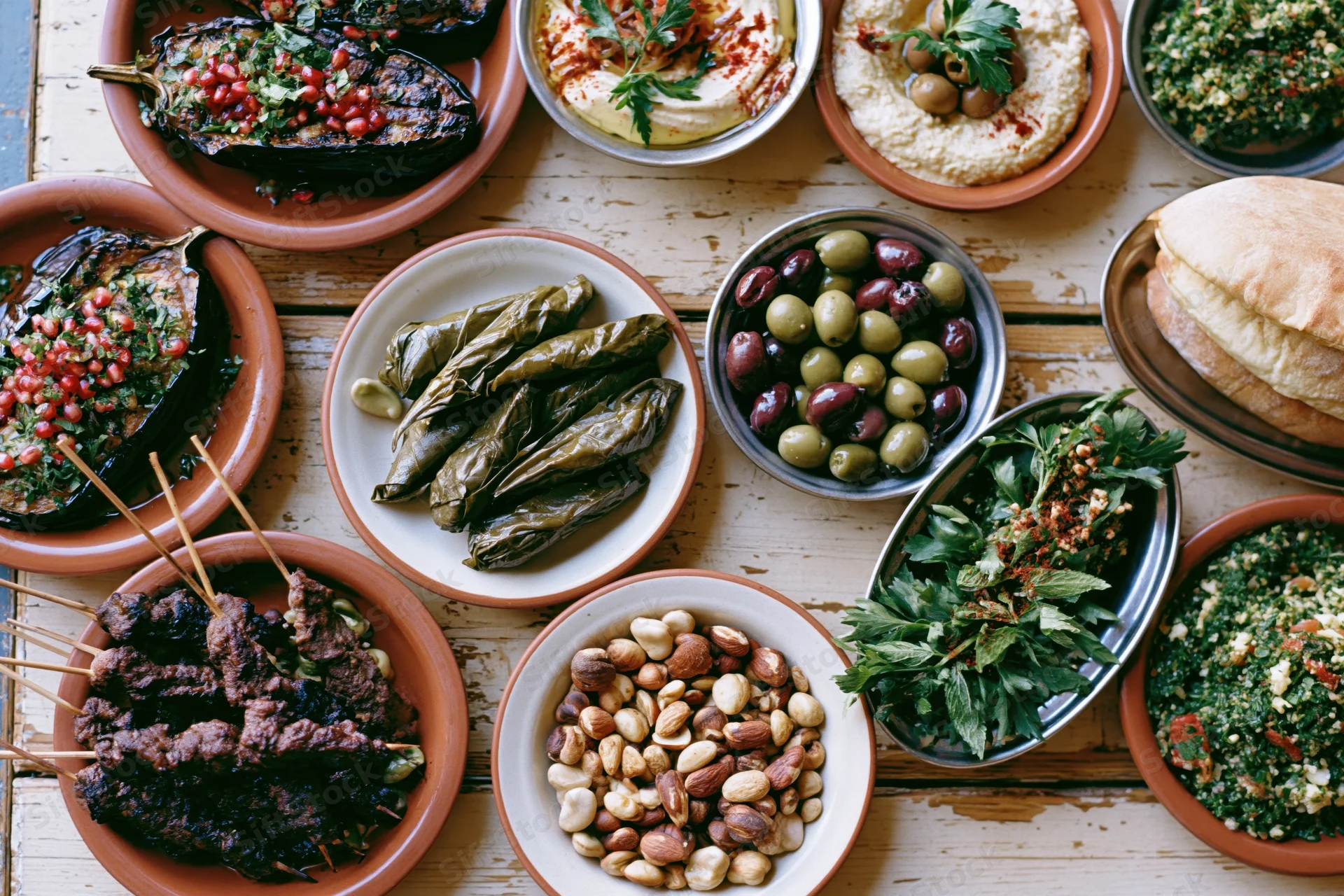 Overhead view of a lebanese mezze spread with grilled eggplant, kebabs, hummus, olives, tabbouleh, and pita on a rustic wooden table