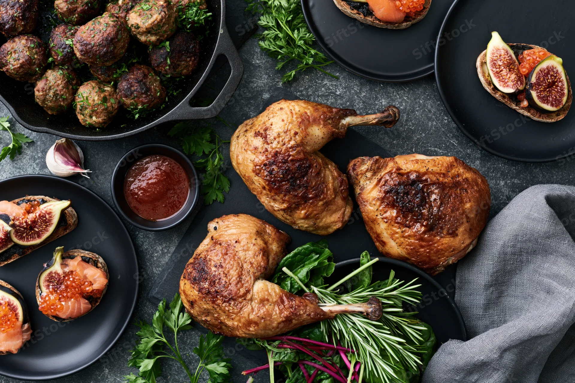 Roasted chicken pieces and meatballs with fig and salmon appetizers arranged on dark slate surface