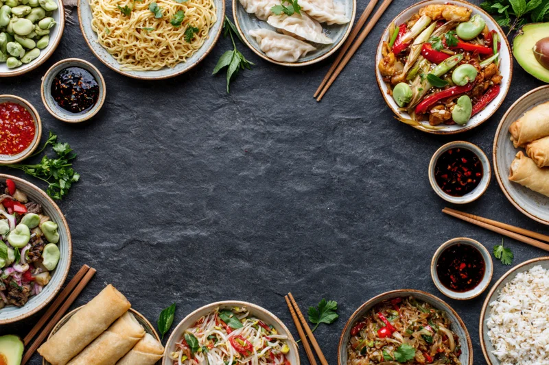 Assorted asian dishes arranged in a circular border on a dark stone surface with copyspace in center