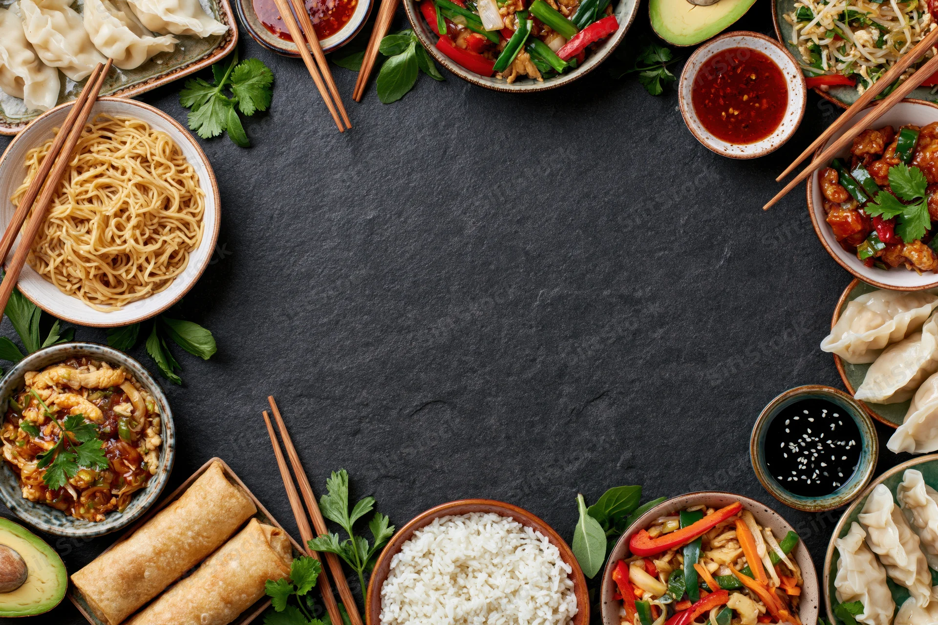 Assorted asian dishes arranged in a circular flat lay on dark slate surface with chopsticks and garnishes