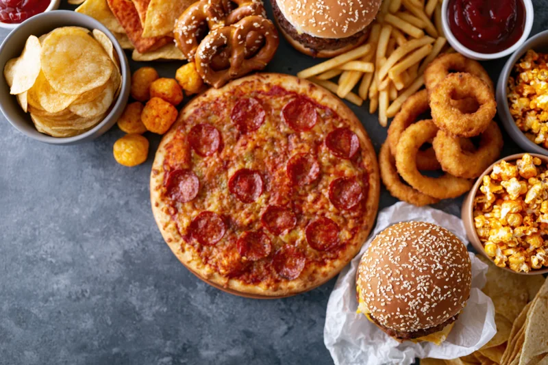 Overhead flat lay of assorted fast food and snacks on a gray textured surface with copyspace