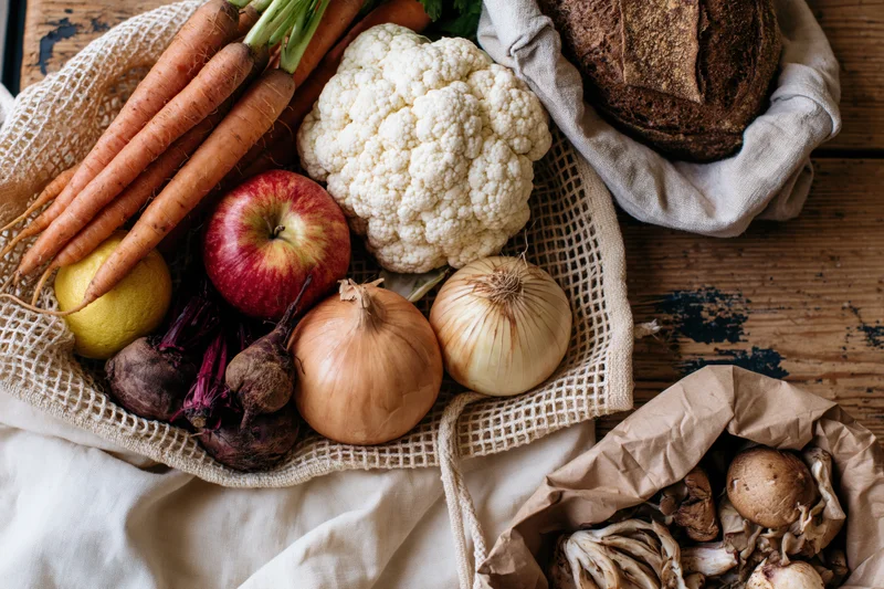 Fresh vegetables and bread arranged in mesh and paper bags on a wooden surface
