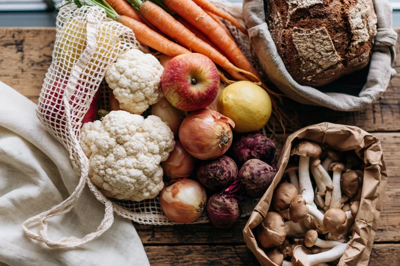 Fresh vegetables and bread arranged in mesh and paper bags on a wooden board