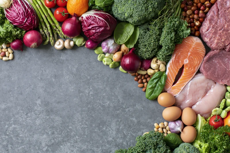 Fresh whole foods arranged in a wide border around a gray surface with copyspace