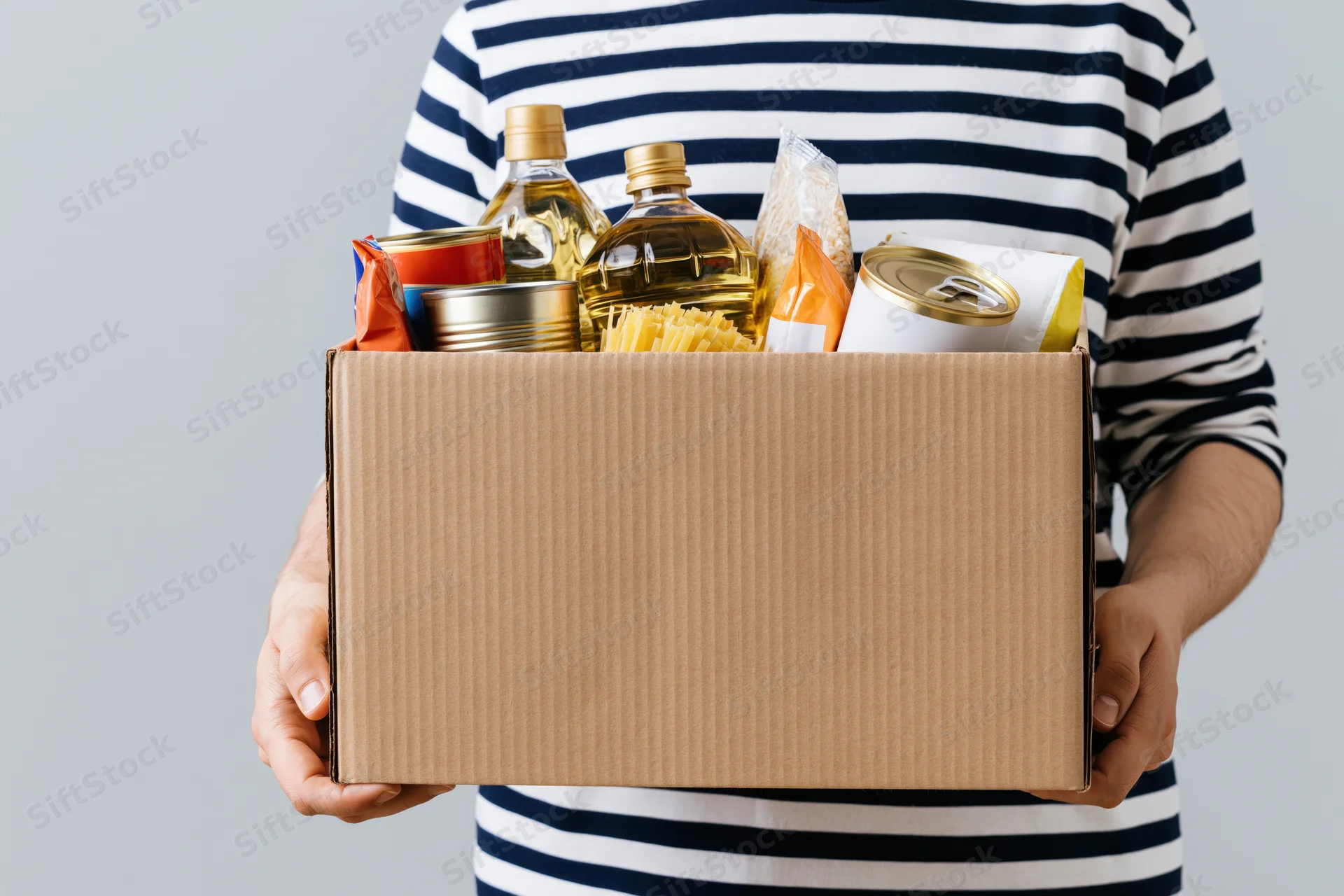 Man holding a cardboard box filled with canned and packaged food items