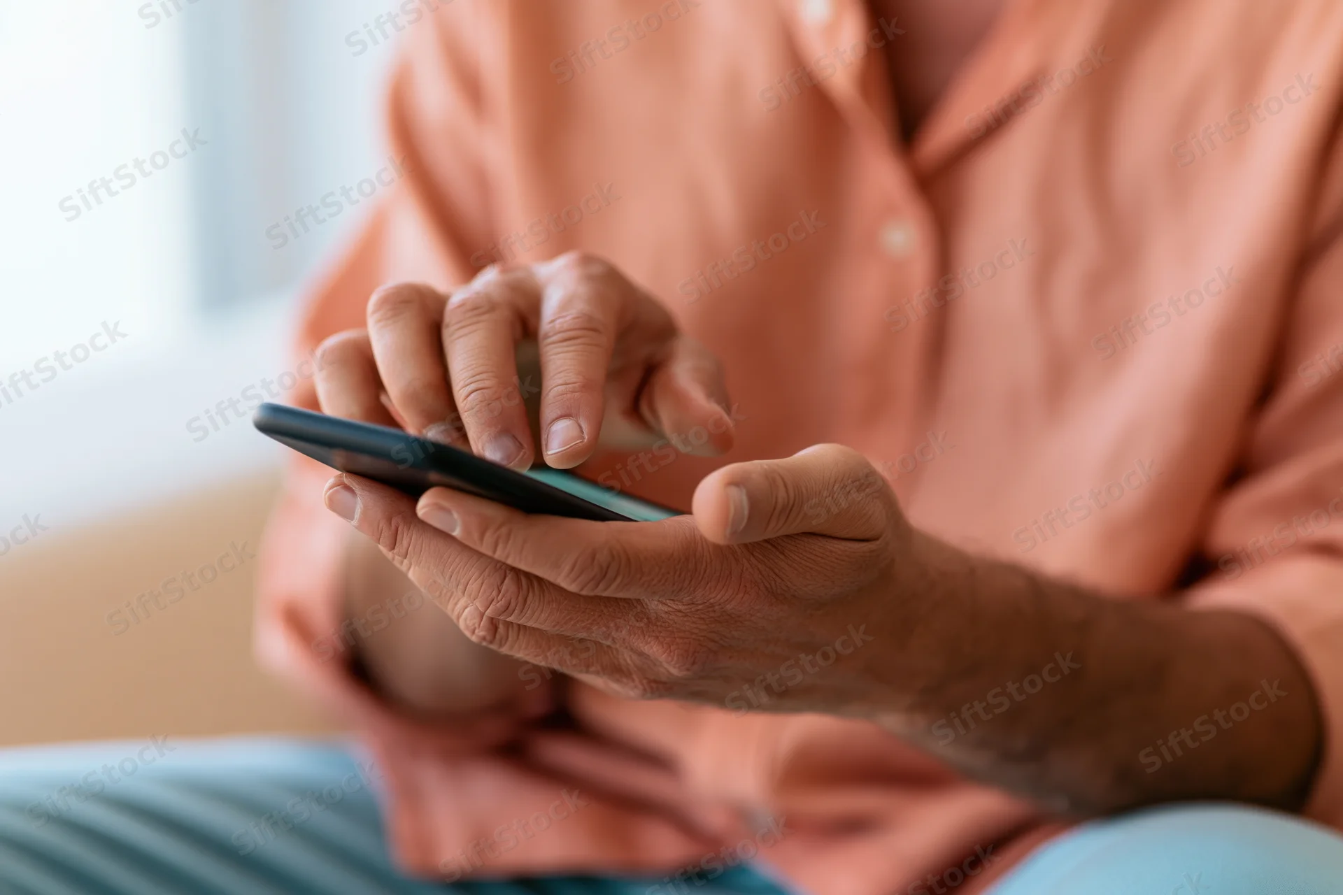 Man tapping smartphone screen with one finger while holding device in both hands indoors