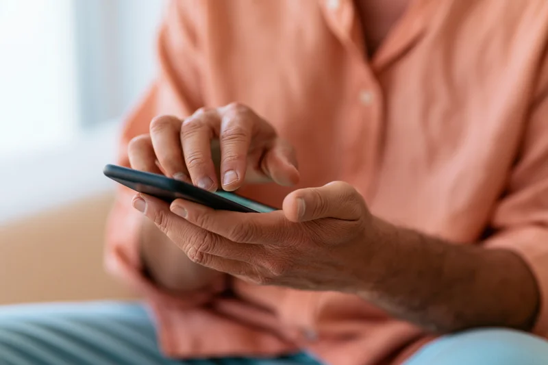 Man tapping smartphone screen with one finger while holding device in both hands indoors