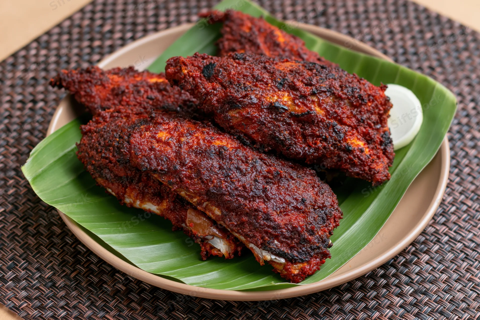 Deep-fried spiced fish pieces on banana leaf served on plate with lime wedge