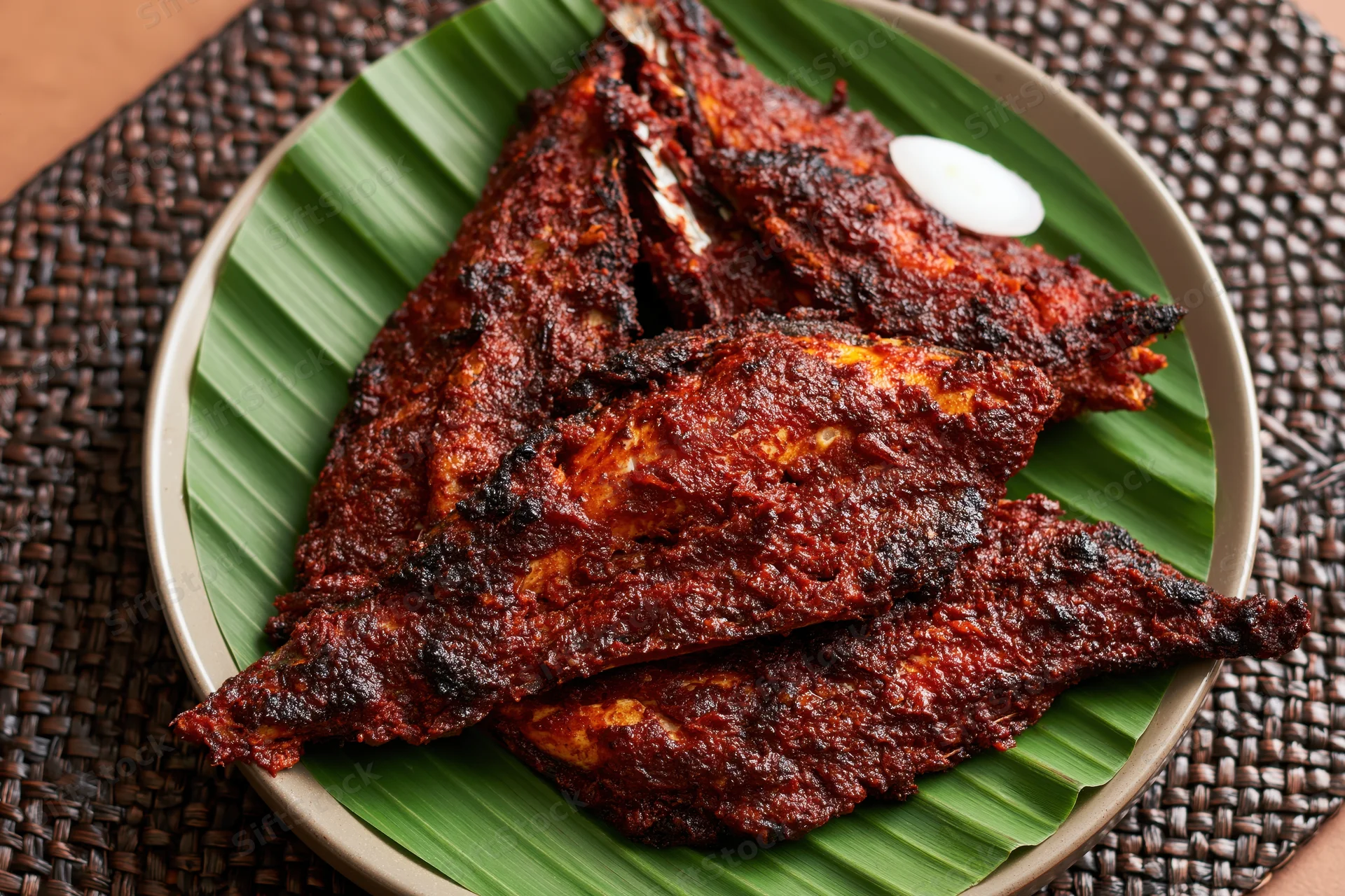 Deep-fried spiced fish pieces served on a banana leaf in a ceramic plate on a woven mat