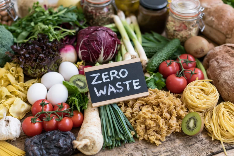 Zero waste sign surrounded by fresh produce and pantry staples on wooden table