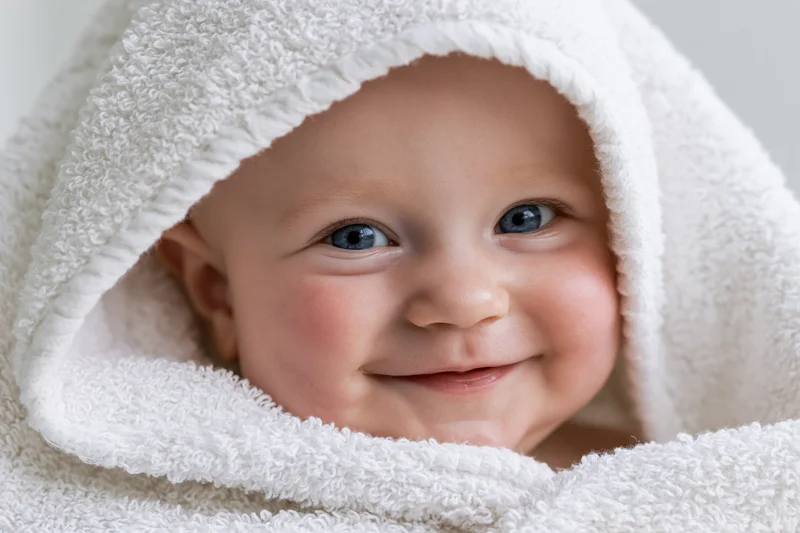 Smiling baby with bright blue eyes peeking from under a white hooded towel
